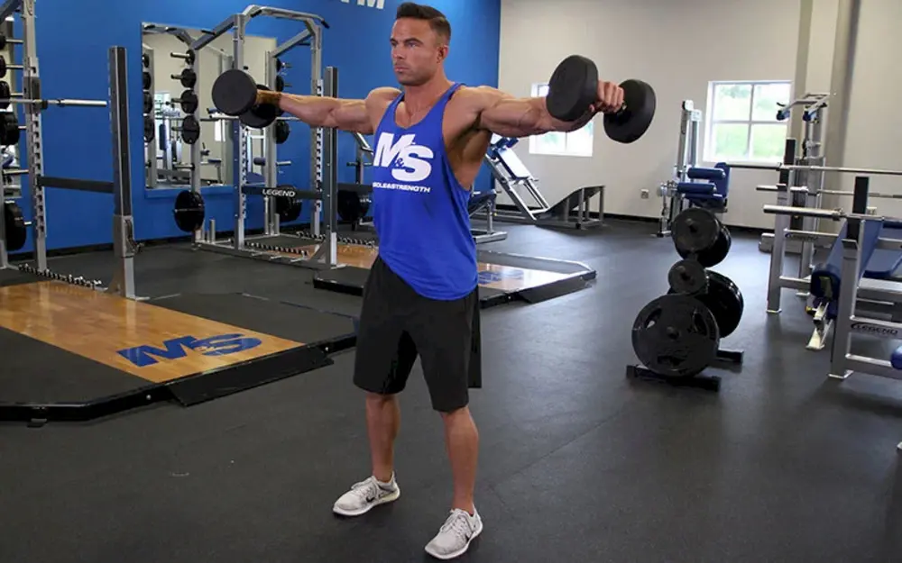 Người đàn ông thực hiện bài tập vai Dumbbell Lateral Raise với tạ đơn tại phòng gym, tập trung vào cơ vai giữa để tăng cường sự rộng và săn chắc cho bờ vai.