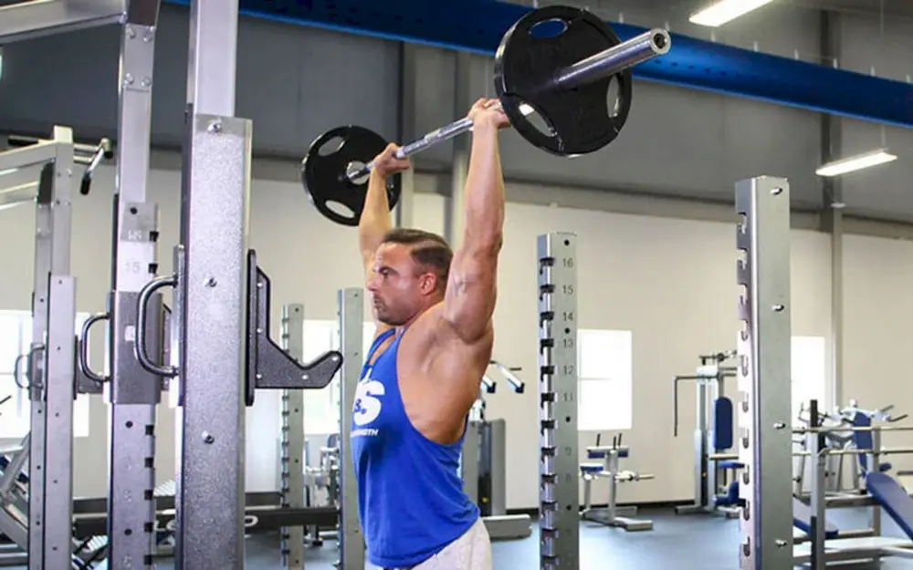 Vận động viên thực hiện bài tập vai Military Press (Overhead Press) với tạ đòn, đẩy tạ qua đầu để xây dựng sức mạnh và kích thước cơ vai toàn diện.
