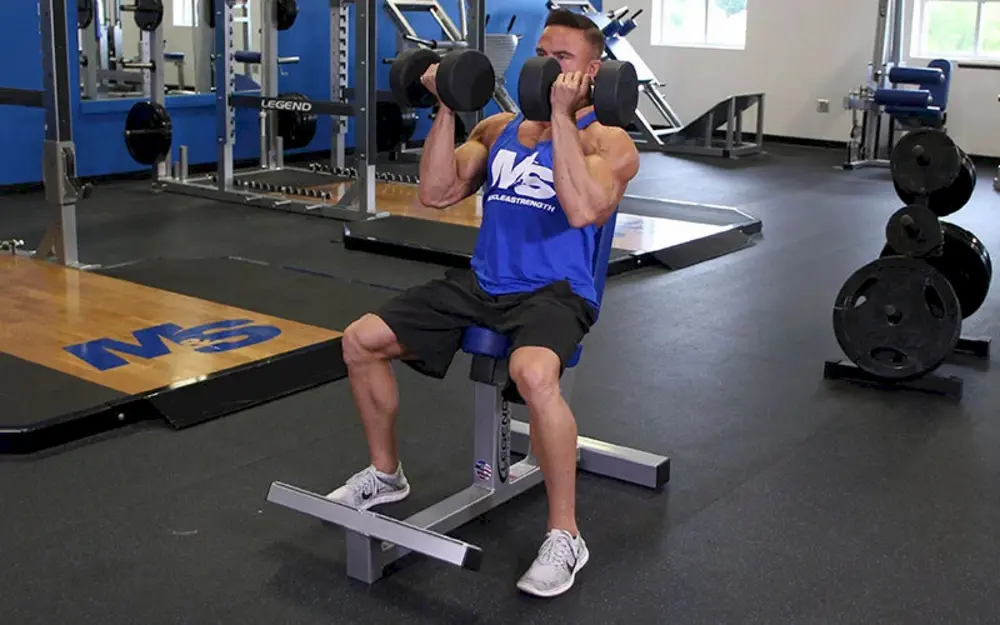 Người tập thực hiện bài tập vai Seated Arnold Press, ngồi trên ghế và đẩy tạ đơn kết hợp xoay cổ tay để tác động toàn diện lên ba nhóm cơ vai.