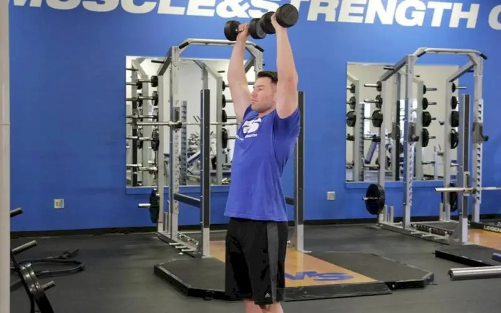 Người tập thực hiện bài tập vai Standing Arnold Press, đứng đẩy tạ đơn qua đầu kết hợp xoay cổ tay, tăng kích thước vai và cải thiện khả năng giữ thăng bằng.