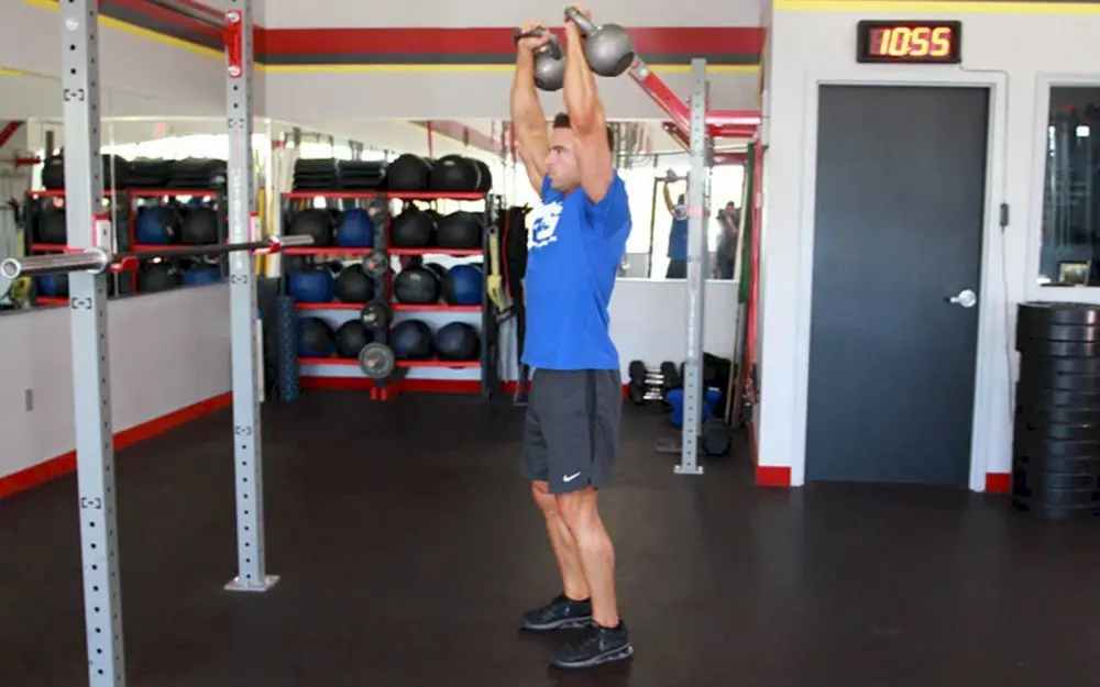 Người tập thực hiện bài tập vai Standing Kettlebell Press, đẩy tạ bình vôi qua đầu để cải thiện sức mạnh và sự ổn định cho vai và cơ core.