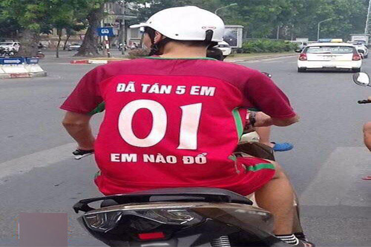 Hai cầu thủ đang đứng cạnh nhau trên sân, một người mặc áo &quot;HAI SÁU TUỔI 01 AI THEO ĐUỔI&quot; và người kia &quot;MƯỜI SÁU TUỔI 99 CON ĐUỔI THEO&quot;, tạo nên một cặp đôi hài hước và độc đáo