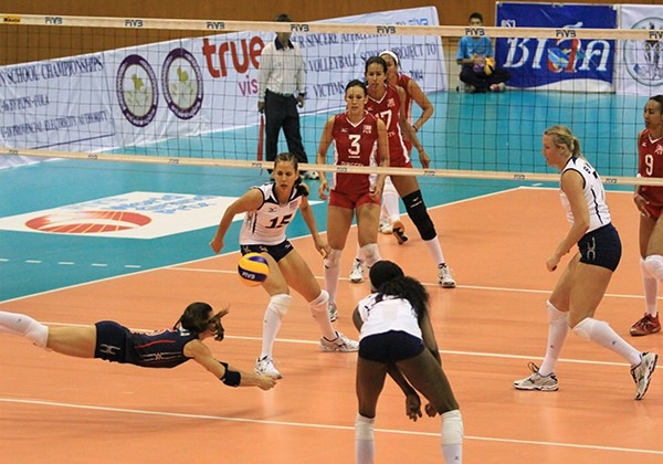 Libero bóng chuyền chuẩn bị đỡ bước một với tư thế thấp, sẵn sàng di chuyển linh hoạt để kiểm soát bóng.