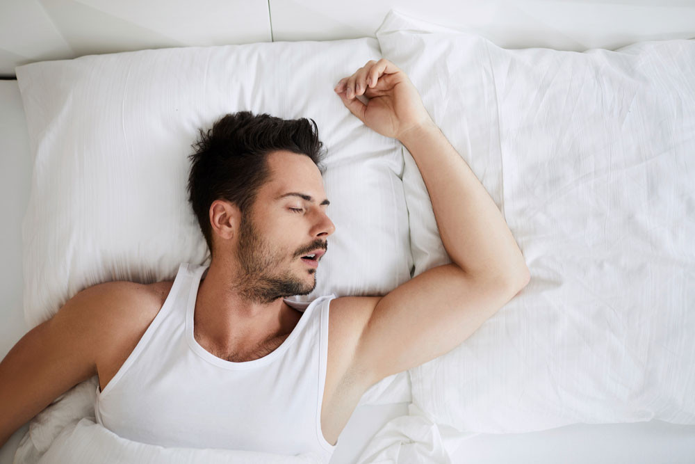 Người đang ngủ say trên giường, minh họa tầm quan trọng của giấc ngủ đúng giờ và đủ giấc để phục hồi thể lực