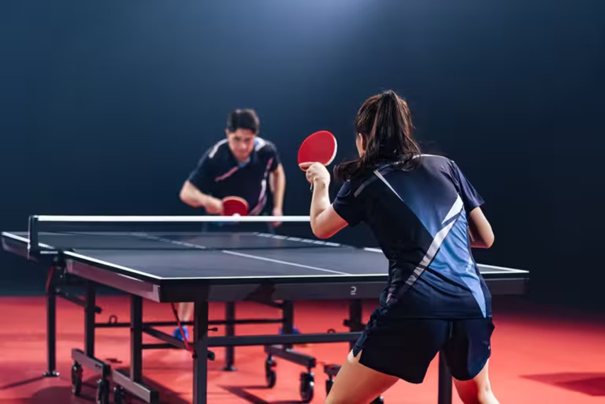 Mô tả cận cảnh một vận động viên bóng bàn nam đang di chuyển trên sân, mặc quần short thể thao nhẹ và linh hoạt